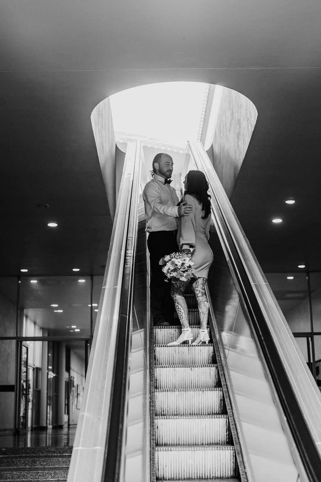 Bay Area wedding photographer captures black and white portrait of bride and groom going up escalator in Marin County Civic Center