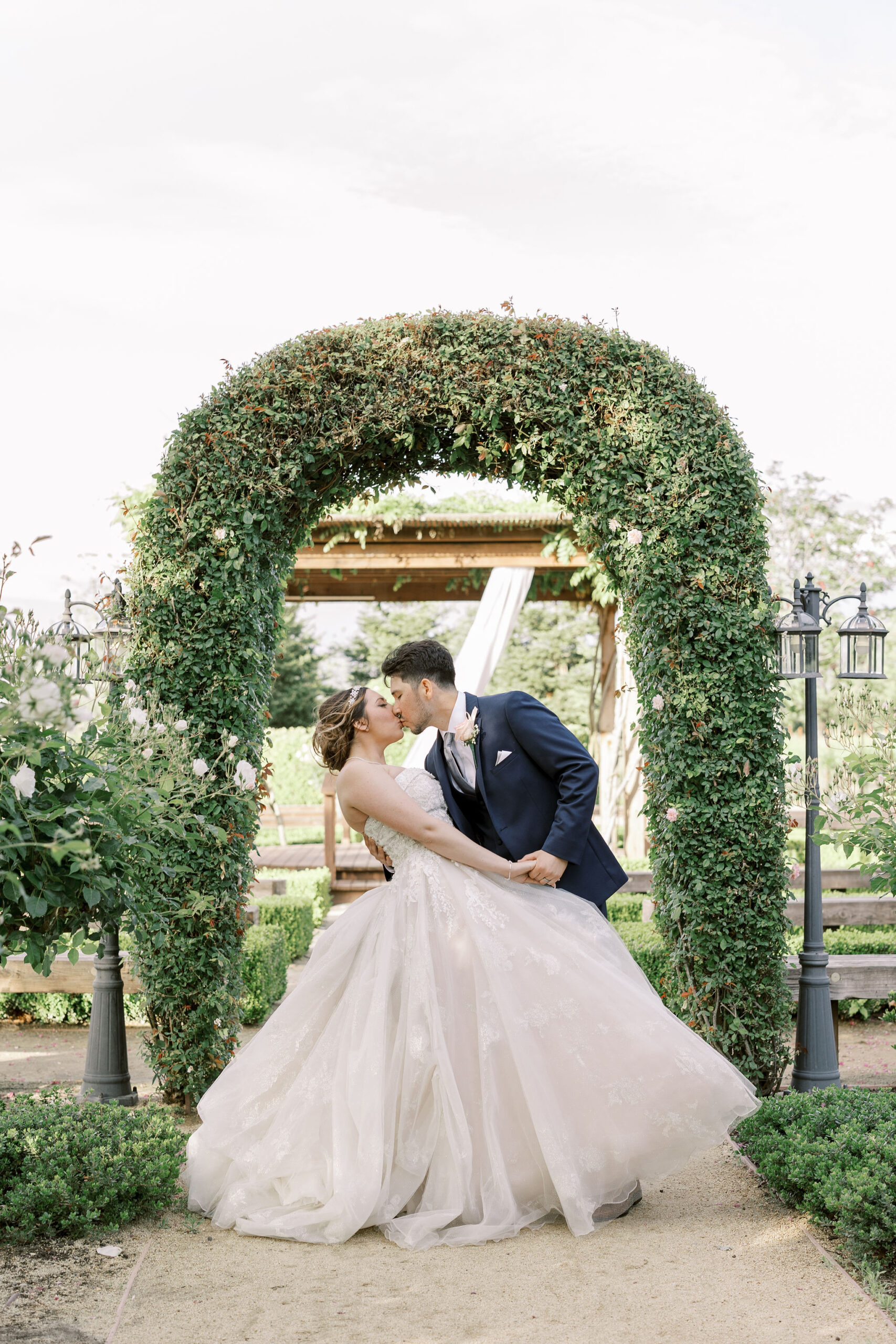 Bay Area wedding photographer photographs bride and groom kissing under a arch made from bushes as the bride leans back