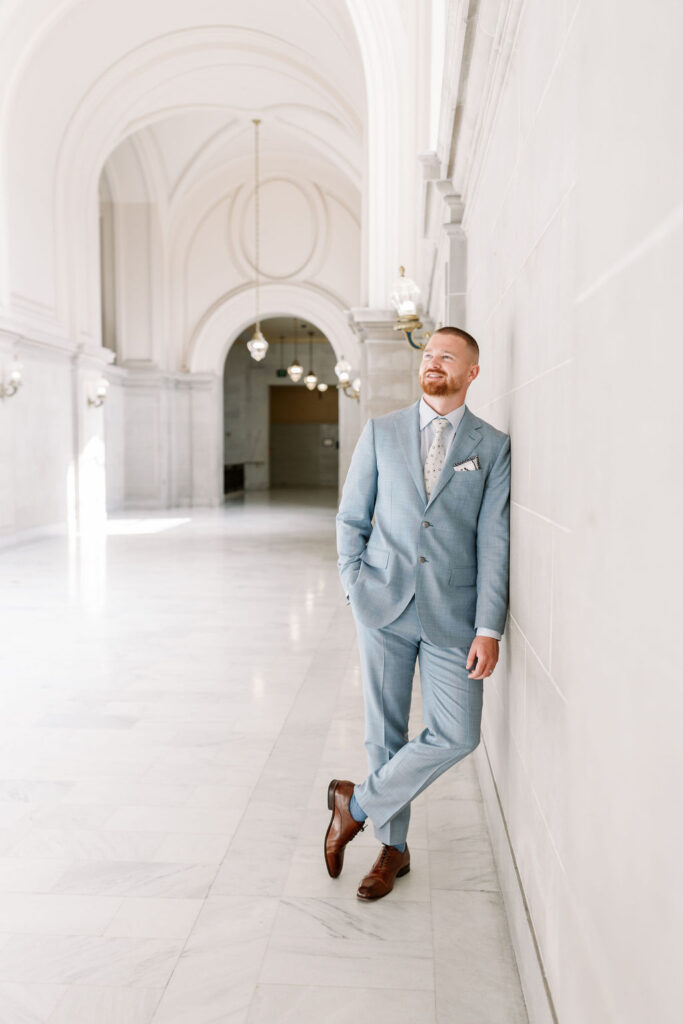 Bay Area wedding photographer captures groom leaning against wall wearing blue suit