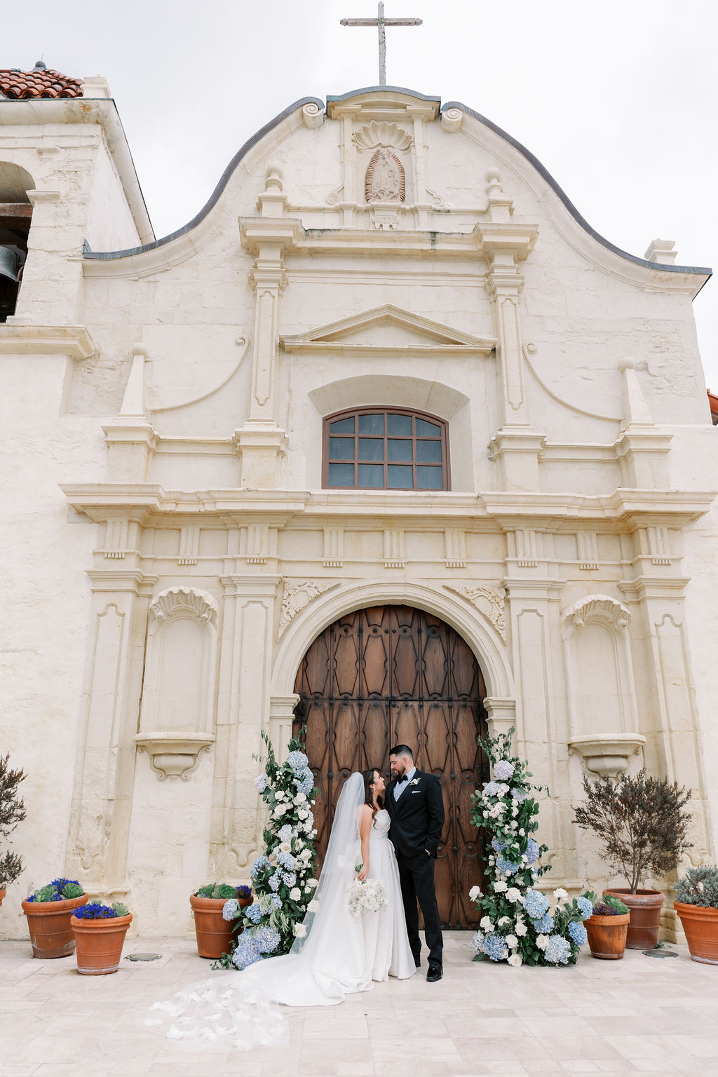 bride and groom kissing in front of San Carlos Cathedral with large floral arches on either side of a dark wood door